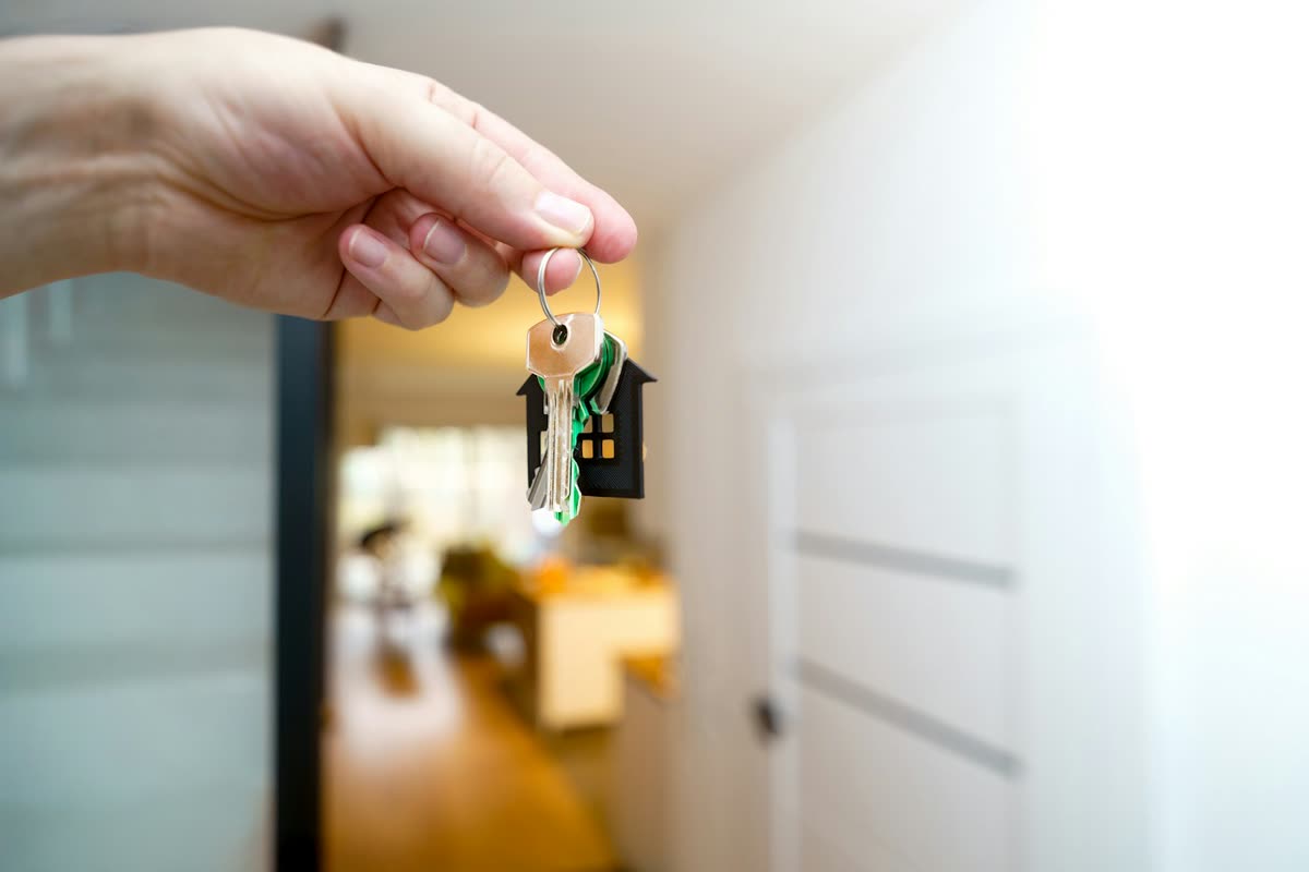 Una mano che porge le chiavi di casa davanti alla porta di ingresso