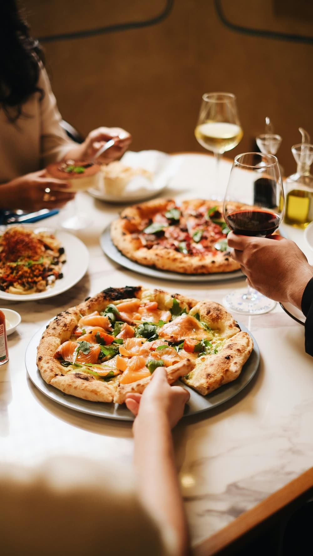 Amici a tavola in pizzeria con due pizze napoletane e calici di vino